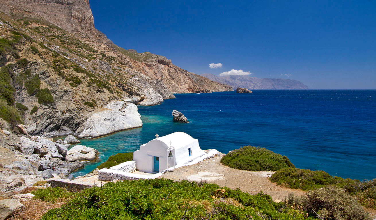 Μικρό λευκό εκκλησάκι μπροστά από τη θάλασσα σε βραχώδεις ακτές