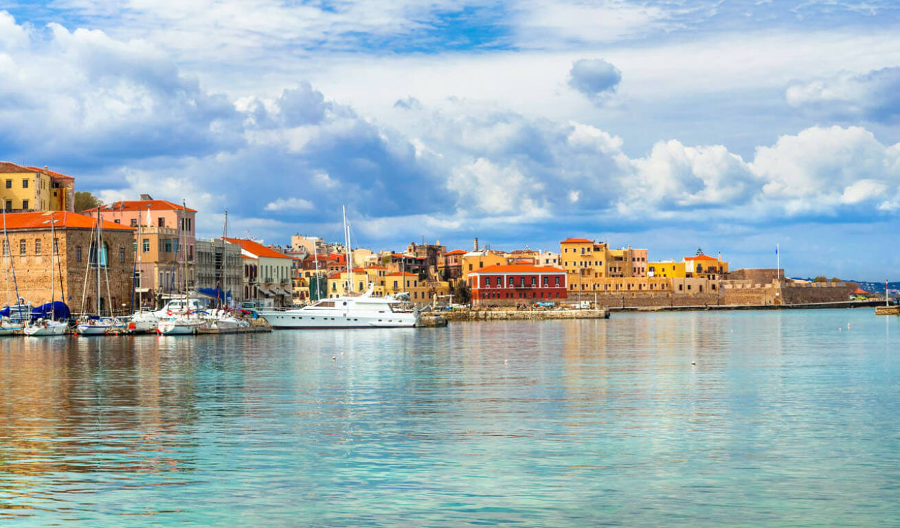 Port with traditional stone and colored buildings, stone lighthouse and sailing boats.