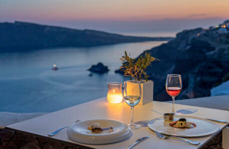 Luxurious food and wine, a lighted candle and a small flowerpot with olive tree overlooking the sea from above at sunset.