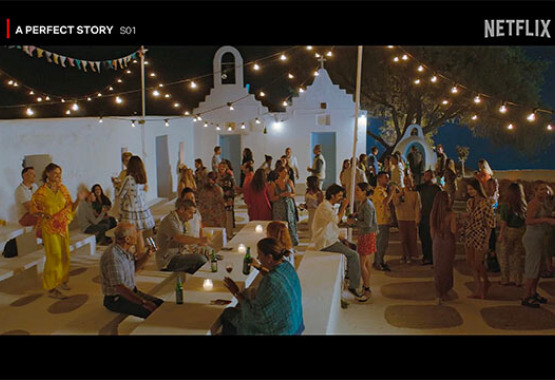 Scene from "A Perfect Story" Season 1 on Netflix showing a group of people at an outdoor evening party with festive lights, near a traditional white building.
