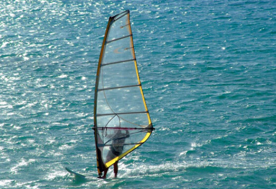 A windsurfer is sailing in the blue sea against the sun.