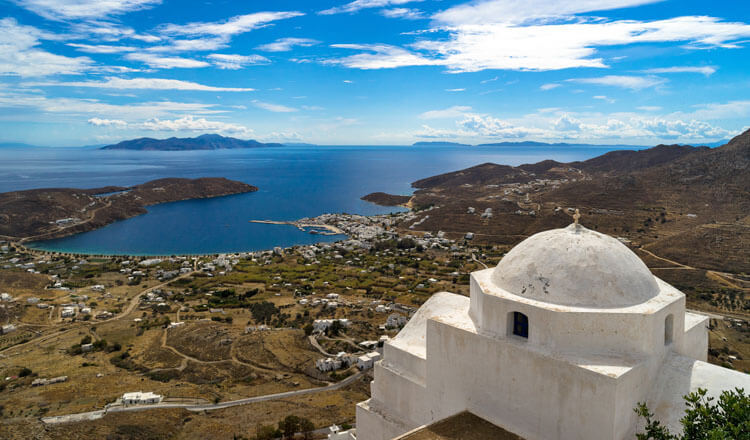 View from above of a large beach with a few houses and a port with a small settlement. White church in the foreground.