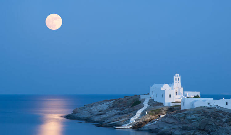 White church on sea rocks with full moon background.