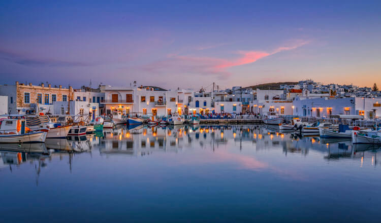 Ήρεμο λιμανάκι με βάρκες περιστοιχισμένο από μικρά άσπρα σπιτάκια και εστιατόρια το δειλινό.