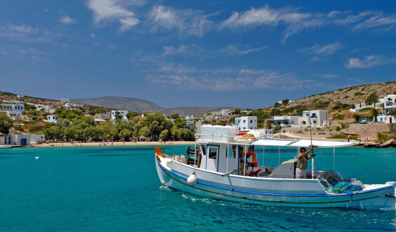 Seaside village of the island with the beach and the whitewasahed houses in the background and a fishing boat in the blue sea