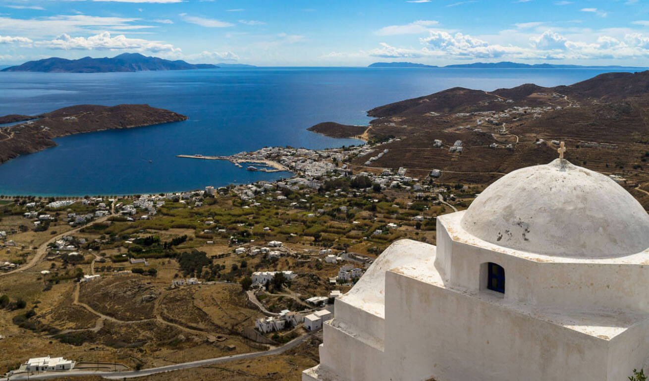 View from above of a large beach with a few houses and a port with a small settlement. White church in the foreground. 