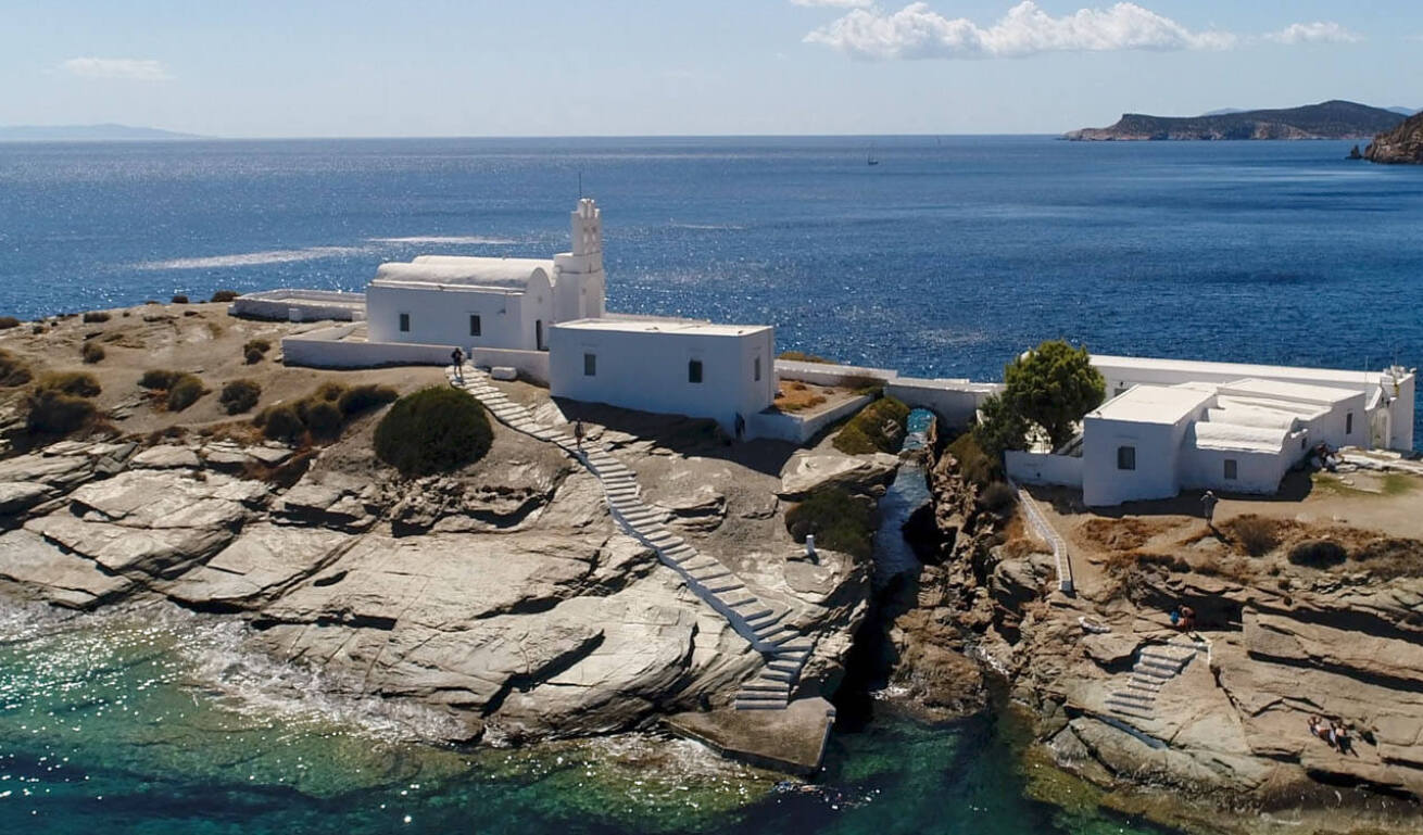 Aerial view of white church on cliffs at sea joined by land with a small bridge. 