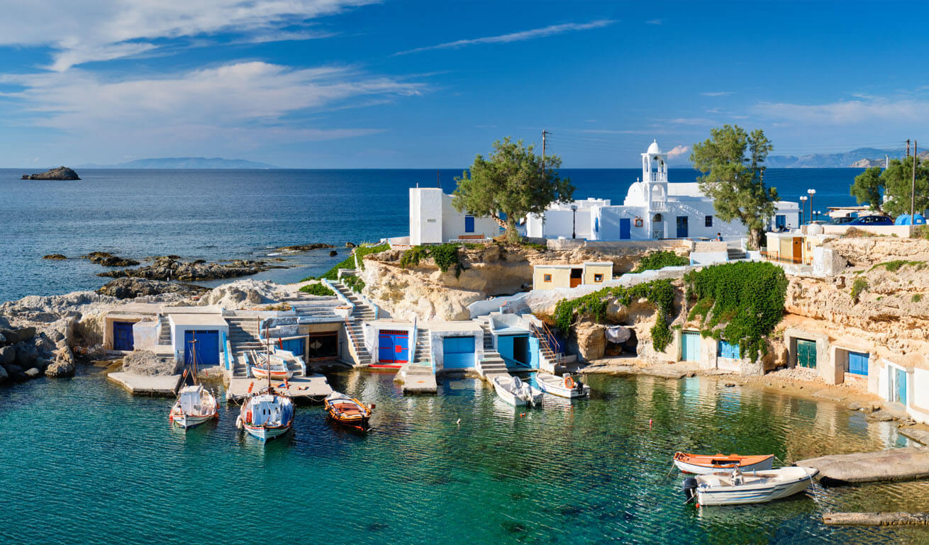 Small bay for boats with small buildings. Above is a white church and in the background the sea. 