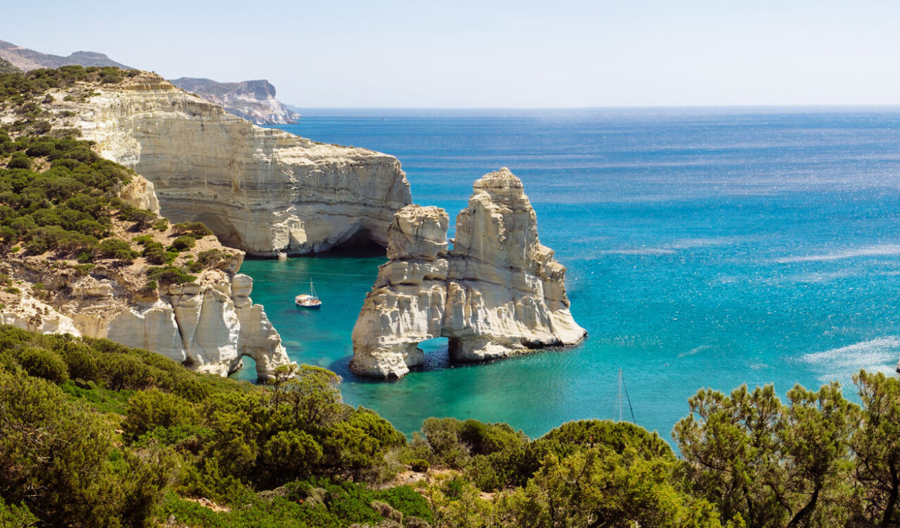 High cliffs above the sea with bushes. Typical large rock with a hole in the sea and next to a small boat. 