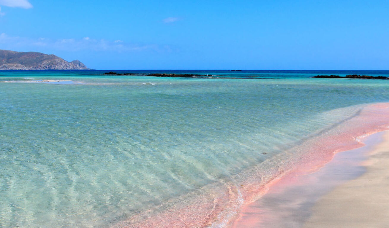 Beach with pink sand and sea with shallow turquoise waters. In the background far land. 
