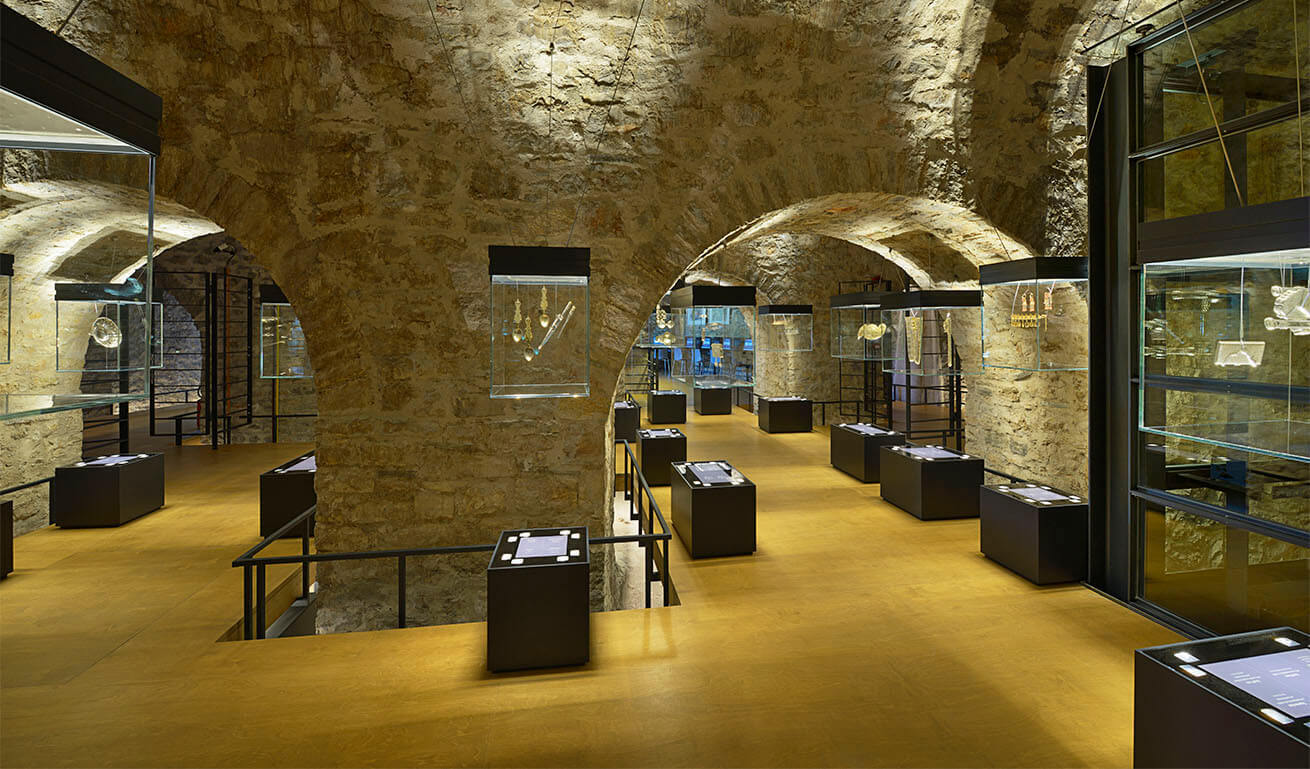 Interior of an old stone building with arches, transformed into a museum with display cases and special lighting.