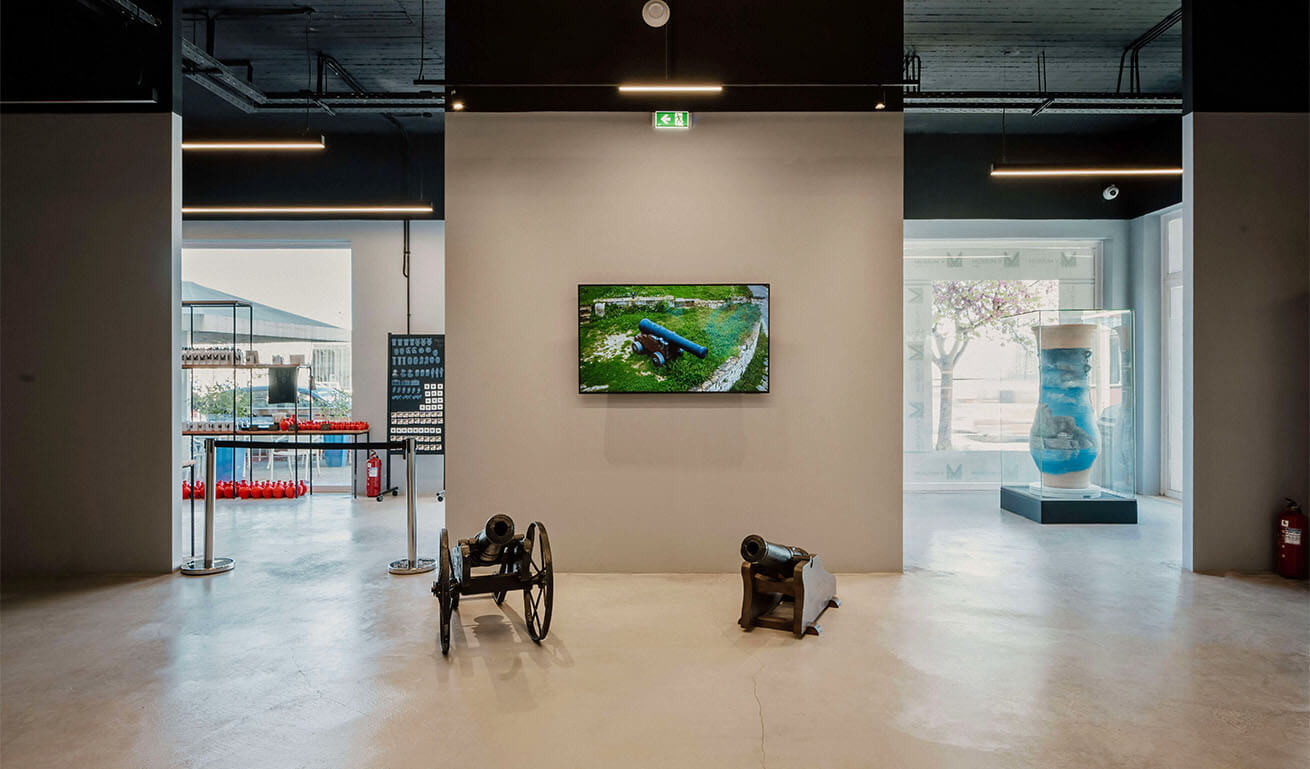 Εσωτερικός χώρος μουσείου με 2 κανόνια και μια εικόνα με κανόνι και 2 ανοίγματα που φαίνεται ένα μεγάλο μπλε ζωγραφισμένο κανάτι και έκθεση μικρών κόκκινων κανατιών.