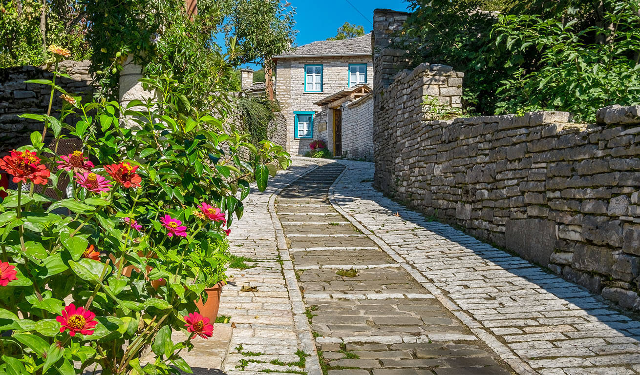Άποψη του ορεινού χωριού Μονοδένδρι με πέτρινο δρόμο, πέτρινα σπίτια και πολλά λουλούδια