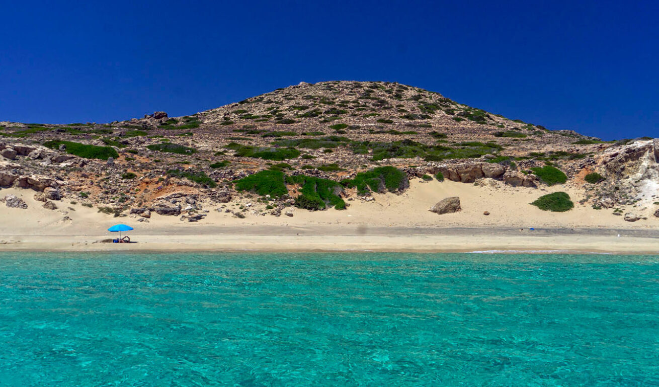 Sandy beach with a view to the greenish blue sea surrounded by rocks