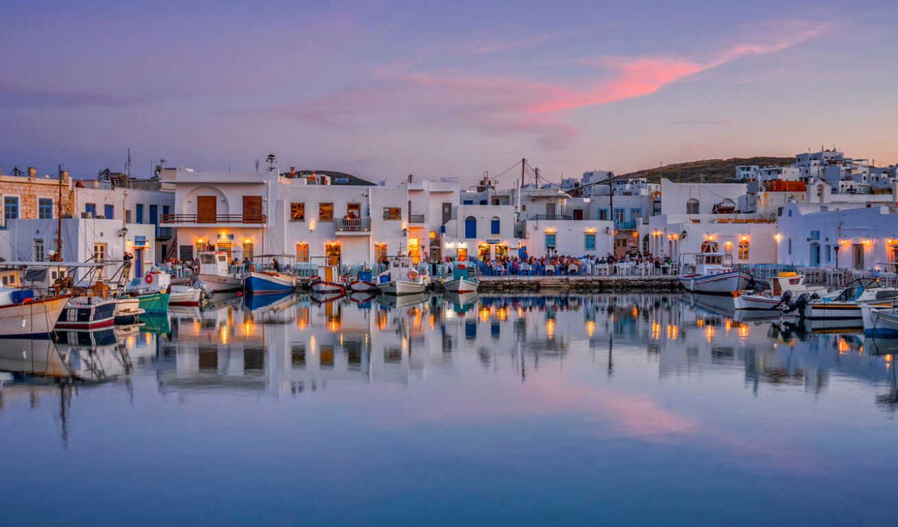 Small and peaceful harbor with boats surrounded by small white houses and restaurants at sunset. 