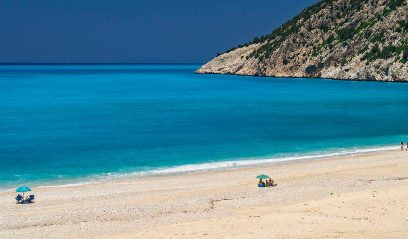 Παραλία με λευκή άμμο και γαλαζοπράσινα νερά και λίγους λουόμενους