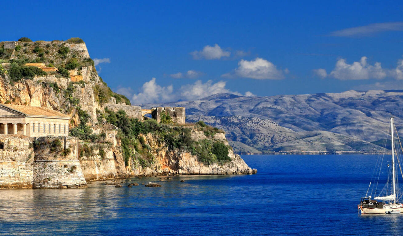 View of the island with the blue sea, the sailing boats around and the steep rocks