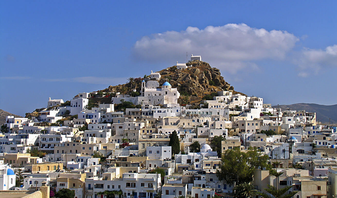 White houses densely built on the slope of a small hill. At the top 3 small churches. 