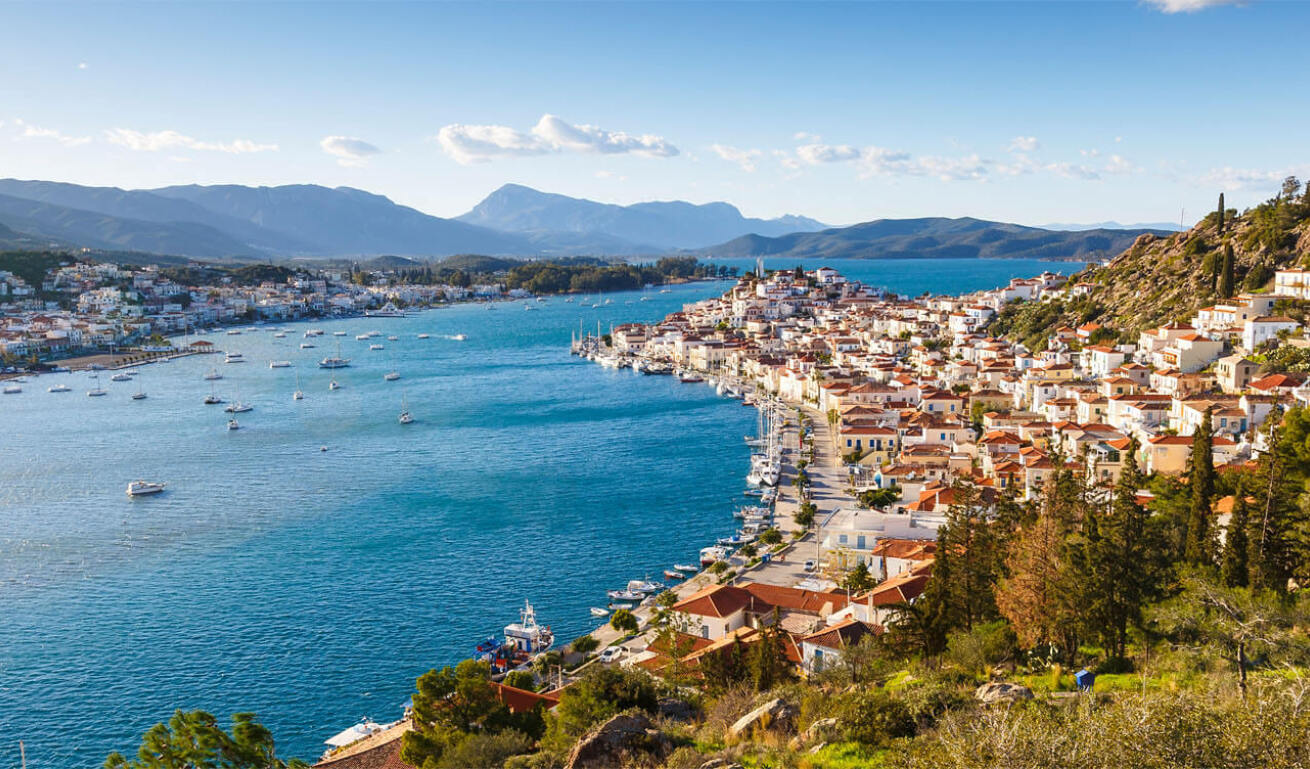 Picturesque seaside village with tiled roofs in front of a canal with small boats and another village on the opposite side.