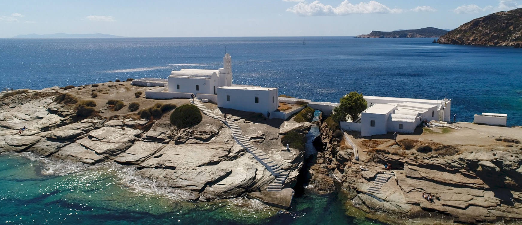 Αεροφωτογραφία από άσπρη εκκλησία πάνω σε βράχια στη θάλασσα που ενώνεται με την ξηρά με ένα γεφυράκι.
