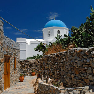 View of a stone-built house and the church of Panagia with the light blue dome is shown in the background 