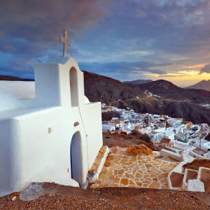 Small white church on top of picturesque settlement in the background dark hills at sunset. 