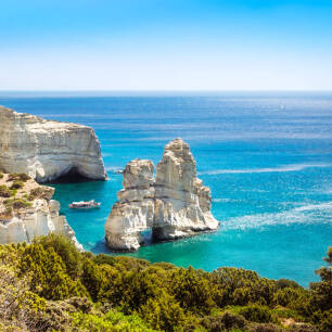 High cliffs above the sea with bushes. Typical large rock with a hole in the sea and next to a small boat. 