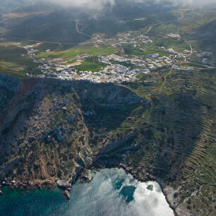 Aerial view of a settlement on a high cliff above the sea with green areas around. 