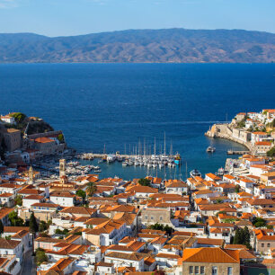View from above of a small bay with small boats surrounded by a traditional settlement with red roofs. 