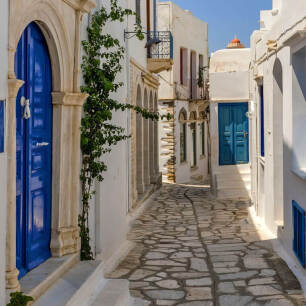 Stone alley in Panormos village, between the traditional houses with the blue doors