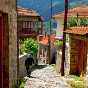 Old man walking down a cobblestone alley lined with stonebuilt houses on a sunny winter day in Metsovo