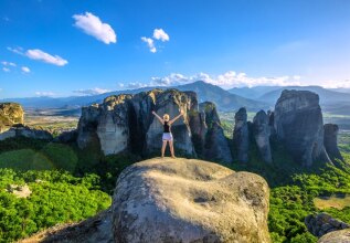 back of a woman with her arms in the air, overlooking the meteora rocks
