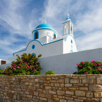 Panoramic view of the whitewashed church of the island with blue dome surrounded by a fence with flowers