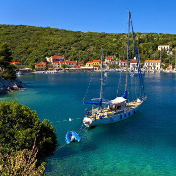 Seaside village with a lot of pine tree and a sailing boat anchored near the port