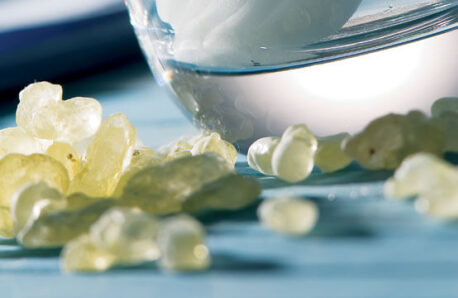 Διαφανείς σταγόνες μαστίχας σε τραπέζι μπροστά από ποτήρι.