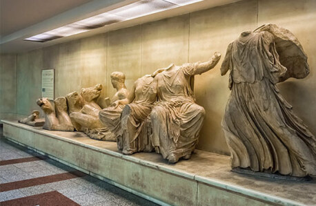 Replicas of ancient statues from the Parthenon frieze in a display case.
