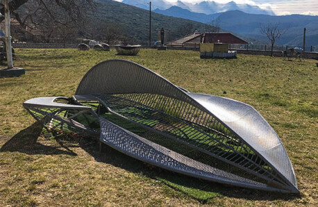 Υπαίθριος χώρος με γρασίδι και σύγχρονα γλυπτά. Χειμώνας και λιακάδα. Στο βάθος μικρό σπίτι με κεραμίδια και τοπίο με βουνά.