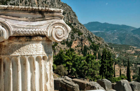 Τμήμα αρχαίας κολώνας με κιονόκρανο. Στο βάθος συνέχεια αρχαιολογικού χώρου και τοπίο με βουνά και δέντρα. 