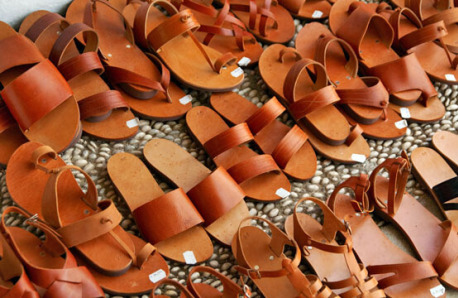Three rows of leather sandals on paved surface with white pebbles. 