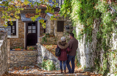 Couple walking on cobbled street between traditional stone houses and plants.