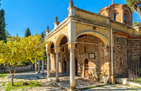 Βυζαντινή πέτρινη εκκλησία με τρούλο και καμάρες στο προαύλιο. Πλακόστρωτη αυλή με μικρό δέντρο. 