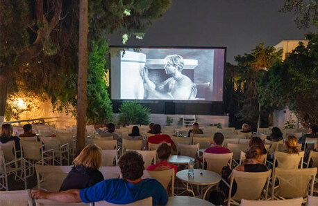 Summer cinema with few people. Trees and plants around. Night.