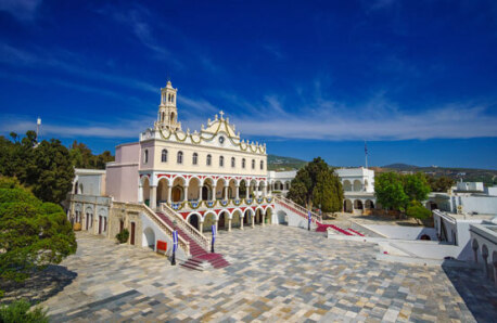 Large church with arches and stairs in a paved courtyard surrounded by trees and other buildings. 