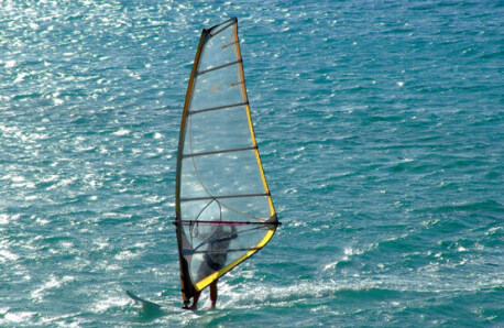 A windsurfer is sailing in the blue sea against the sun.