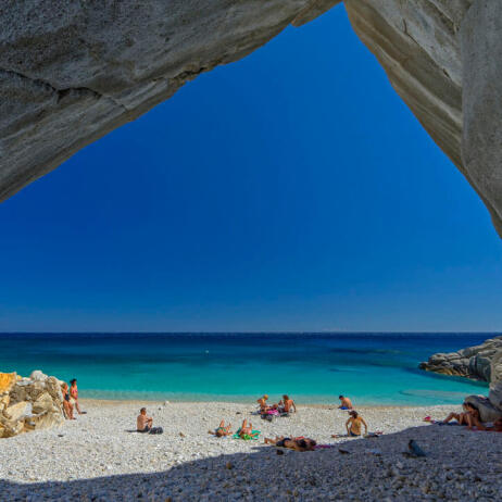 Beach with white stones and turquoise waters. People in swimsuits on the beach. Rocks around like a cave. 