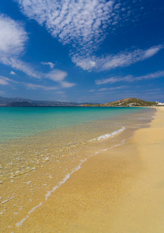 Yellow sandy beach with calm turquoise sea and low hills in the background. 