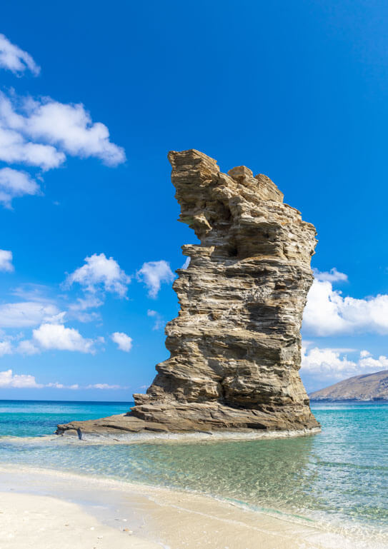 Sandy beach with a large vertical rock in the sea. 