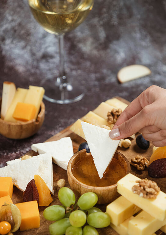 Dipping cheese into honey. Platter, snacks and white wine. Overhead