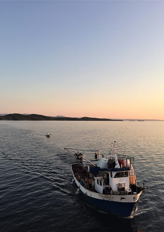 A fishing boat floating on calm waters during sunset with hills in the background.