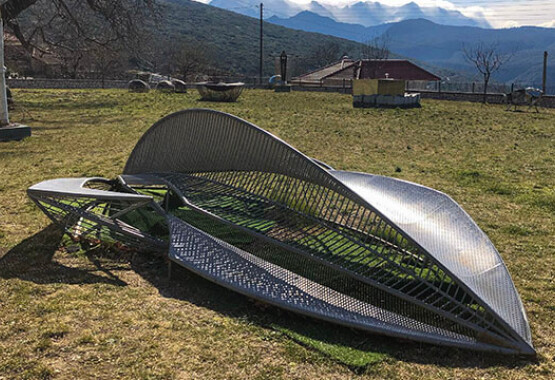 Outdoor area with grass and modern sculptures. Winter and sunshine. In the background small house with tiles and landscape with mountains.